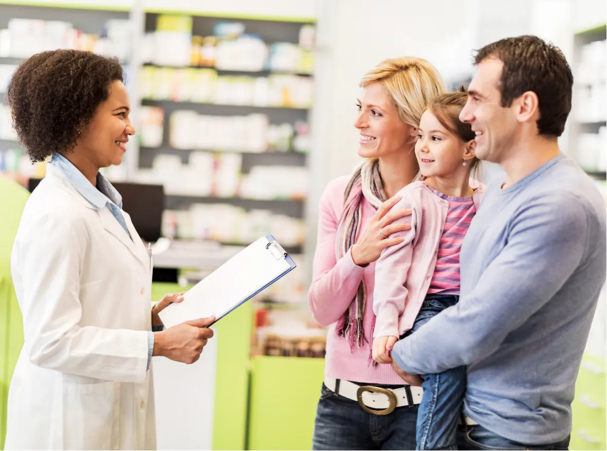 A pharmacist smiles and talks with a family of three at the pharmacy counter.