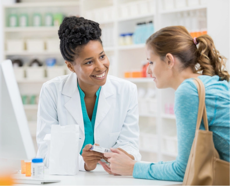 Female pharmacist smiling and helping a customer at a pharmacy counter with medication.
