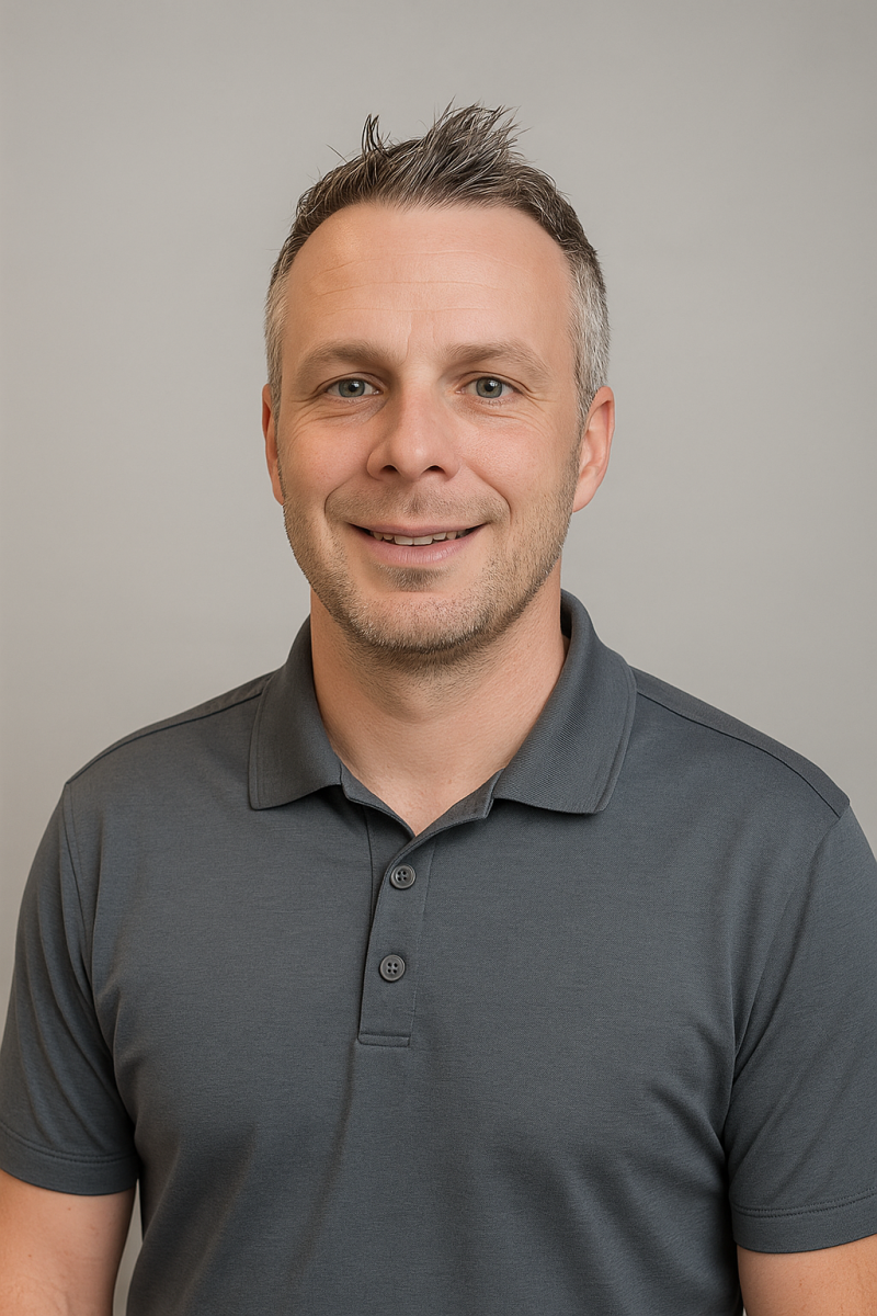 Smiling man with short hair wearing a charcoal gray polo shirt, posing in front of a plain light background.