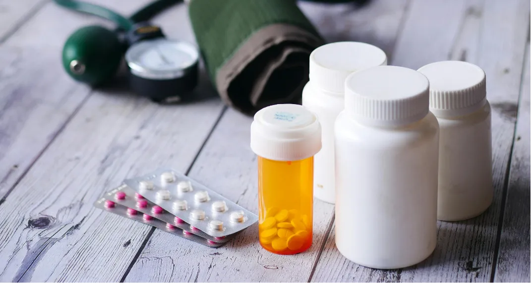 A gloved hand holds blood samples, while a nurse attends to a patient in the background.