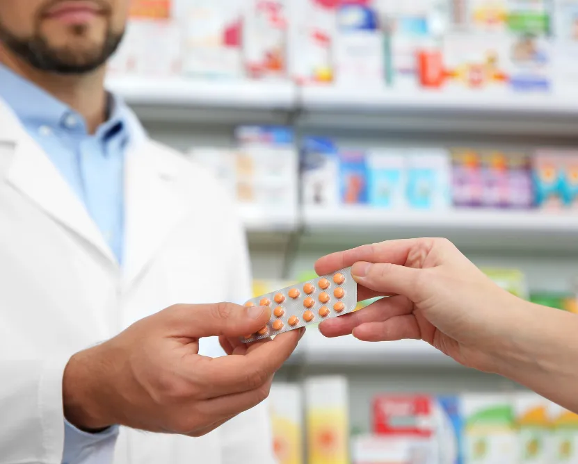 refill-1 Pharmacist handing a blister pack of pills to a customer in a pharmacy.