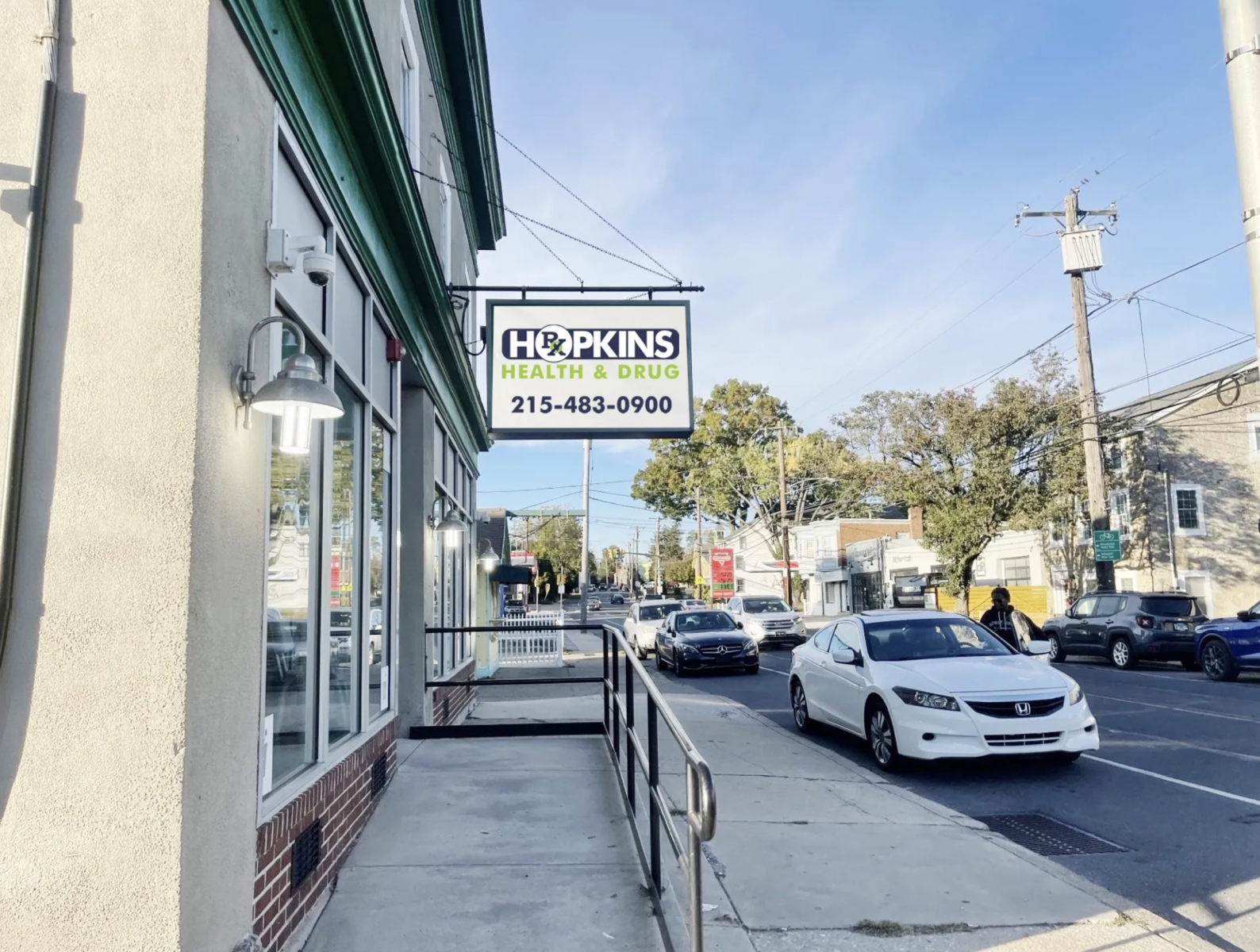 Screenshot 2025-05-22 at 7_43_09 PM A sidewalk view of Hopkins Health & Drug storefront sign with cars parked along the street.