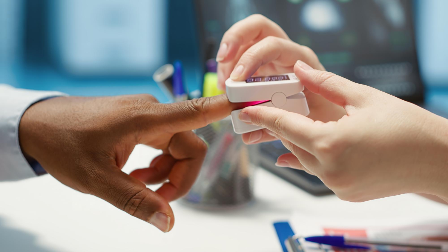 116452 A person places a pulse oximeter on another person’s finger in a medical office setting.