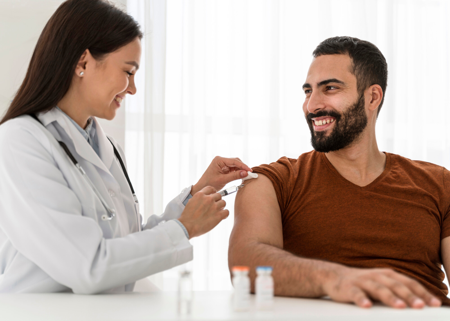 2148755571 Smiling nurse gives a vaccine injection to a cheerful man sitting in a clinic.